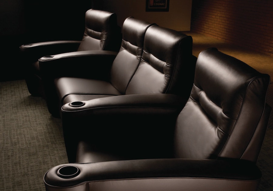 Row of plush black leather home theater recliners with cup holders in the armrests, set in a dimly lit media room.