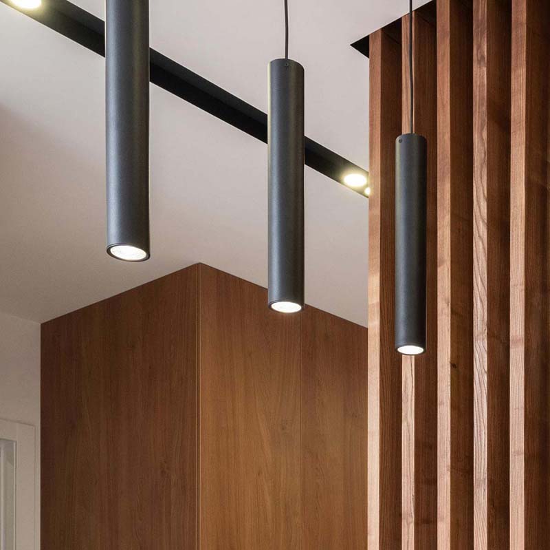 Black cylindrical pendants suspended from a ceiling, set against a wooden accent wall in a contemporary interior.