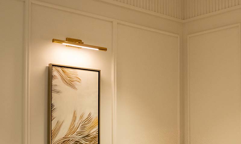 a gold lighting fixture pointing light towards a piece of artwork