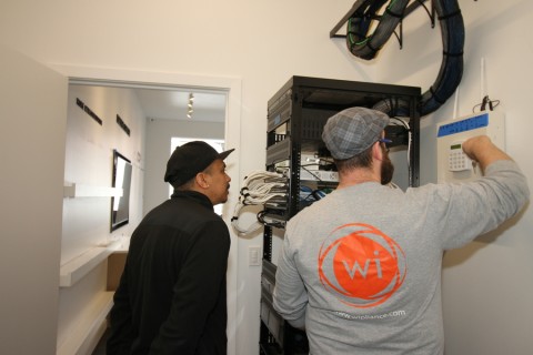 two Wipliance technicians work on an AV rack and keypad in a client’s hallway