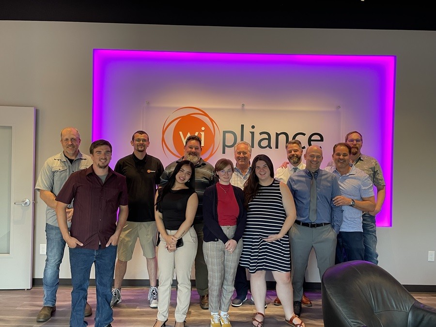 Wipliance team posing in front of the Wipliance logo in the new Spokane design center. 