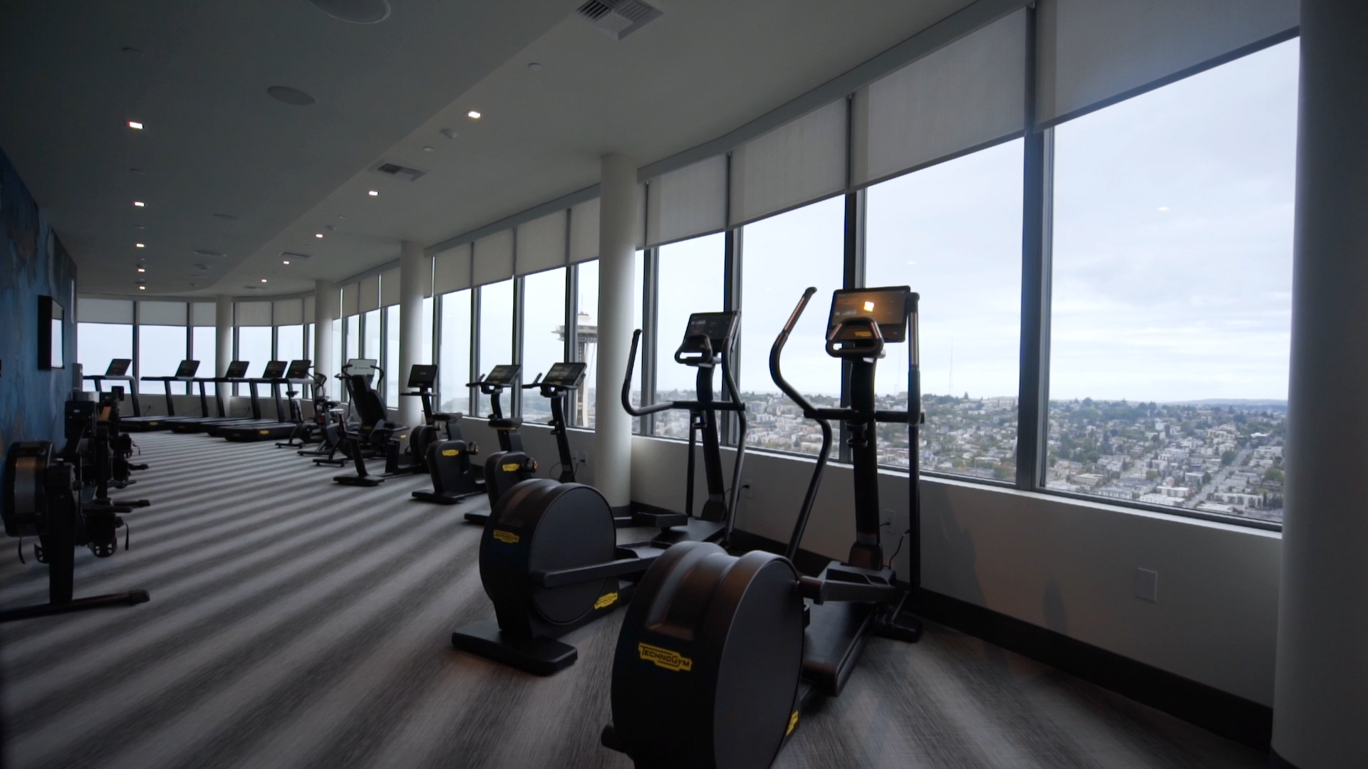 High-rise fitness room with cardio equipment and large windows showcasing the Seattle skyline.