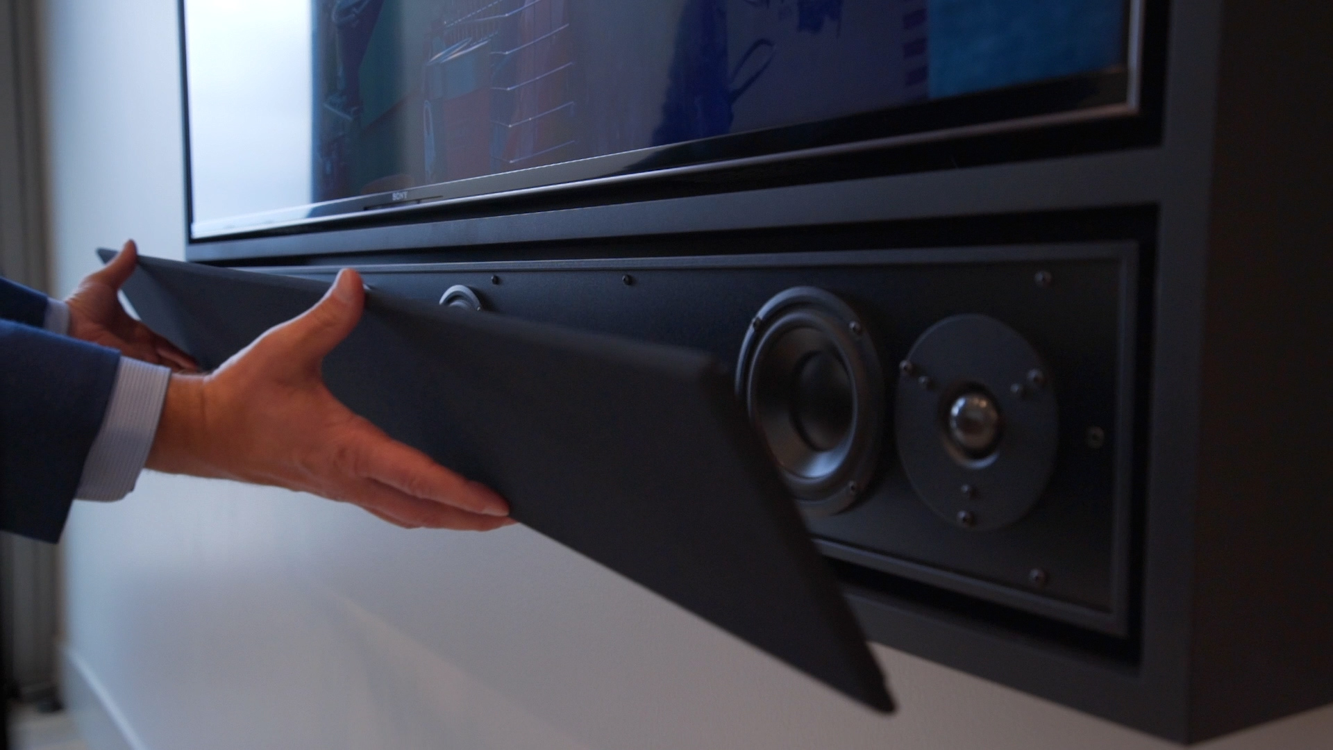 Close-up of a sleek wall-mounted TV and custom speaker system with a hidden speaker cover.