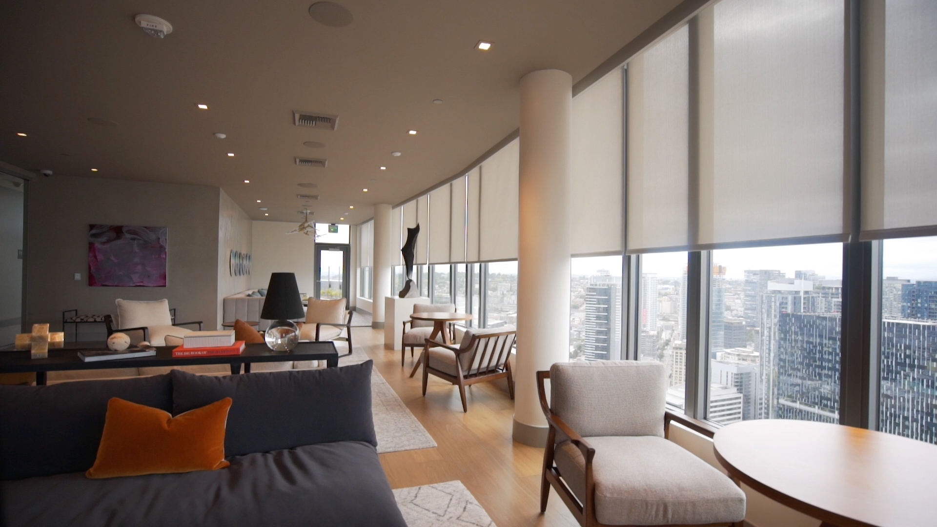Modern living space with floor-to-ceiling windows and shades, offering city views in a high-rise.