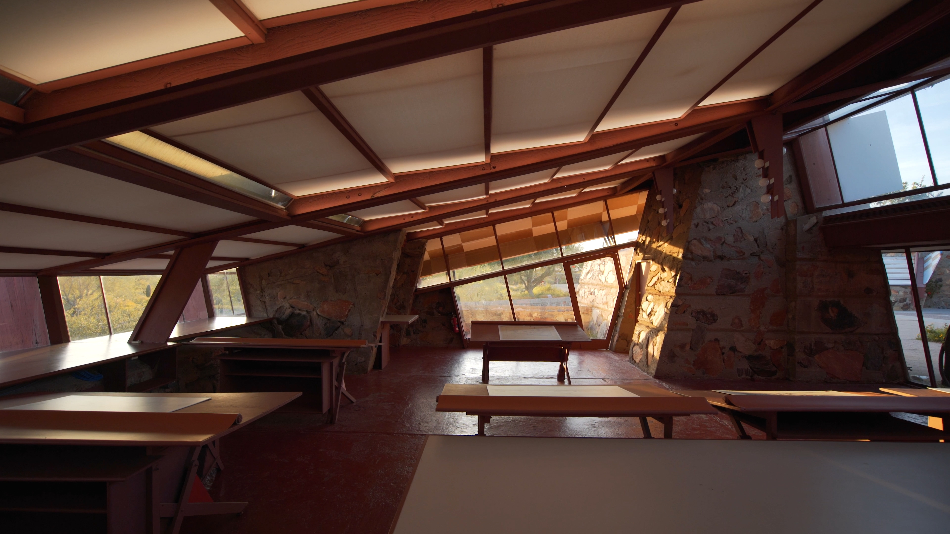 Daylight-filled drafting studio at Taliesin West with angled windows, wooden work tables, and soft LED ceiling panels.