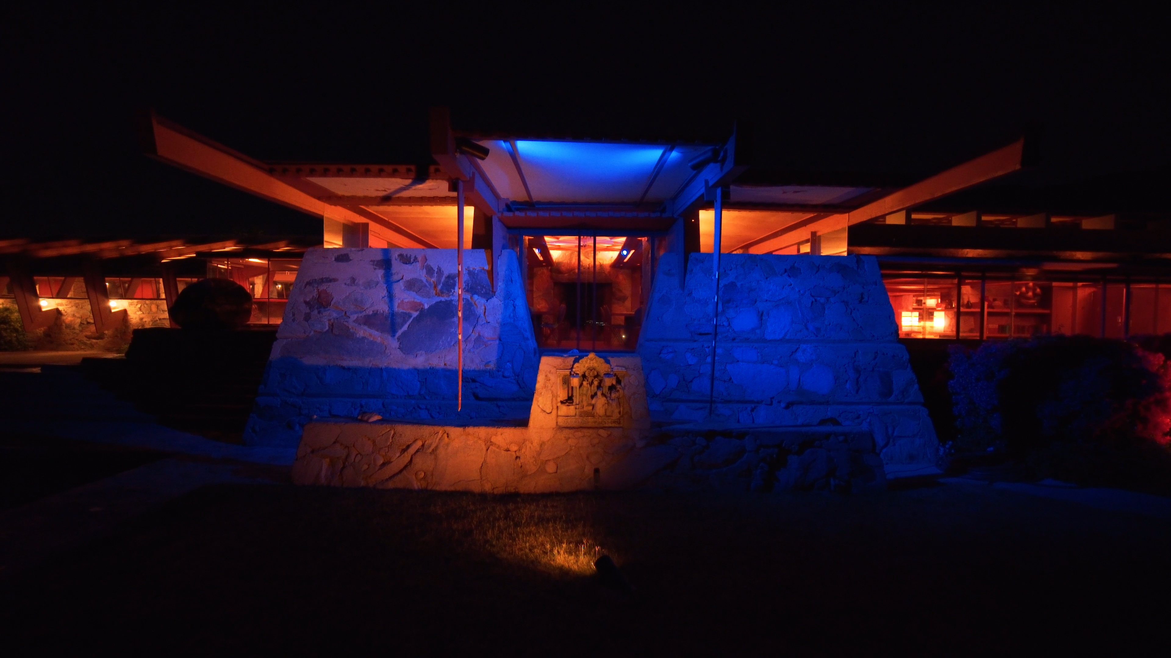 Night view of Taliesin West entrance with dynamic blue and orange LED lighting highlighting stone architecture.