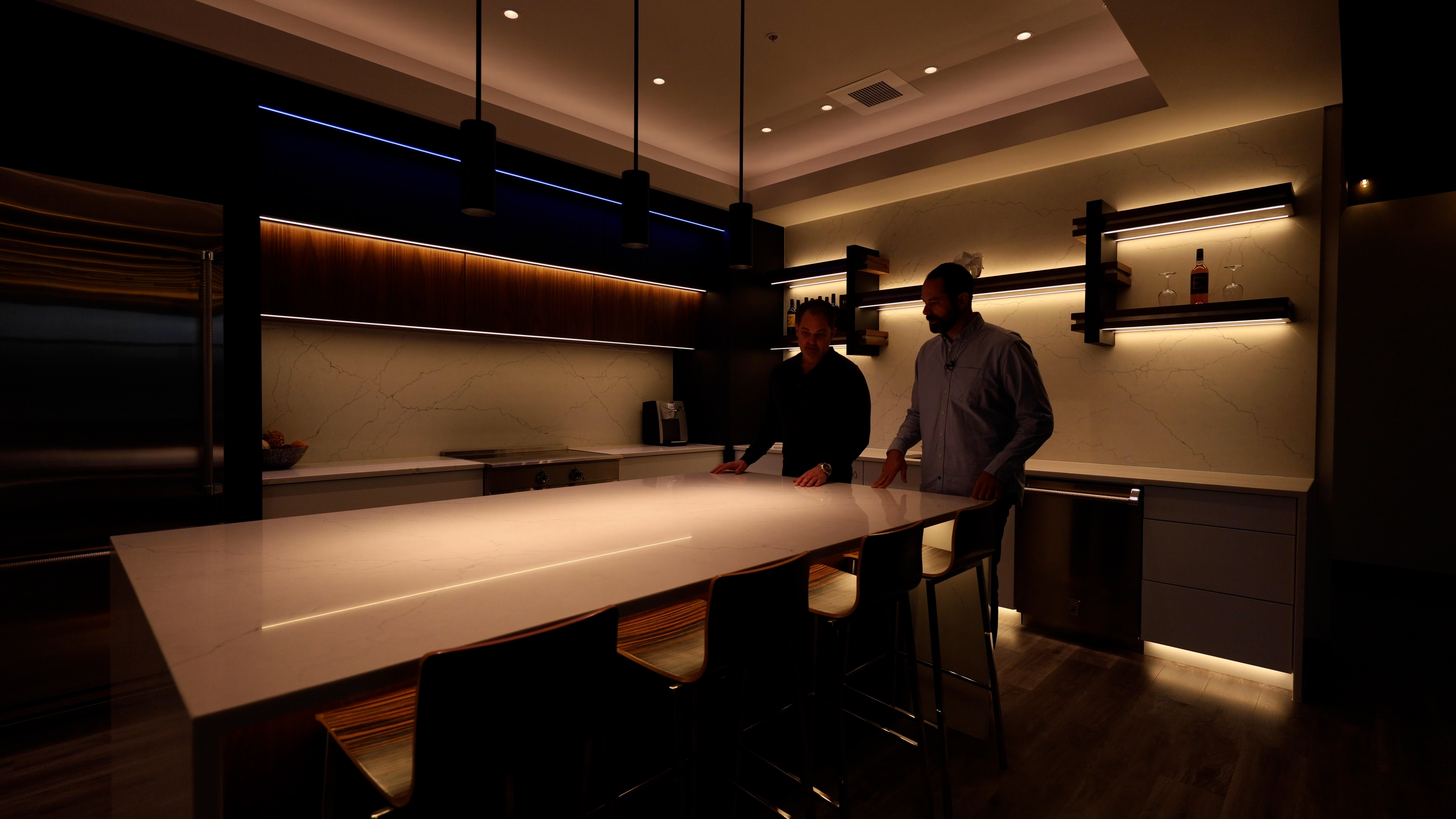 Two people adjusting and testing DMF lighting systems in a luxurious kitchen with subtle lighting accents.