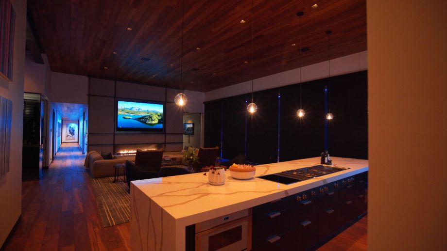 In a modern living space, a sleek smart home remote rests on a glass table with a wooden coaster.