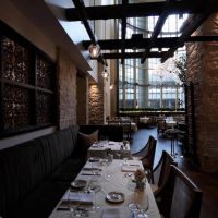 Elegant restaurant dining room with layered pendant lighting, stone columns, and a sunlit atrium skylight.