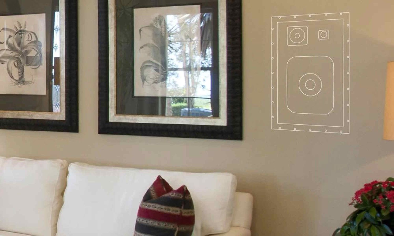 Hidden speaker diagram on a wall next to framed art above a white sofa