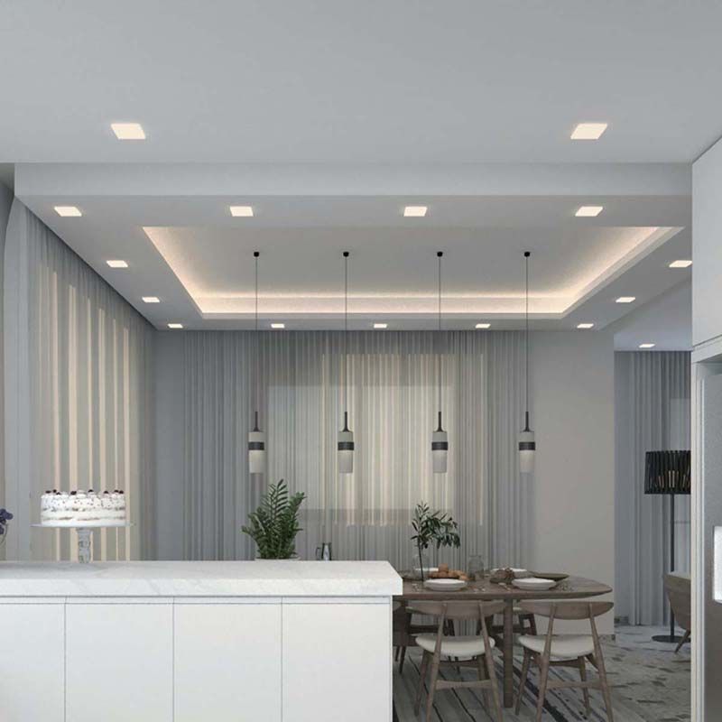 Modern kitchen and dining area featuring multiple recessed fixtures in a white ceiling, along with suspended pendant lights.